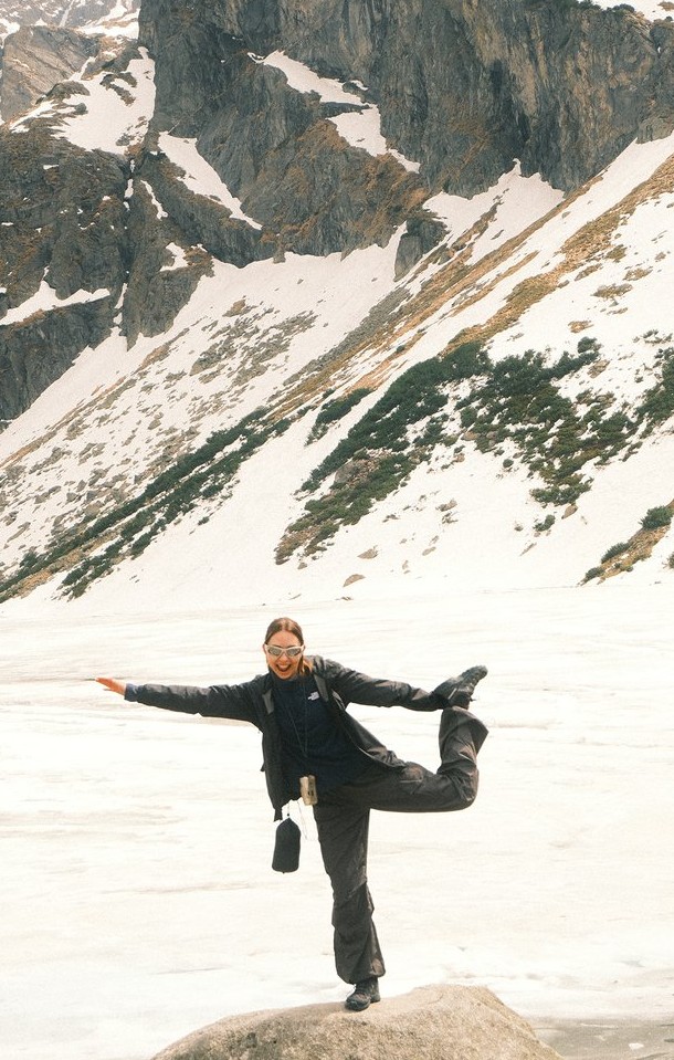 Yuliya balancing on a rock in front of a snowy mountain